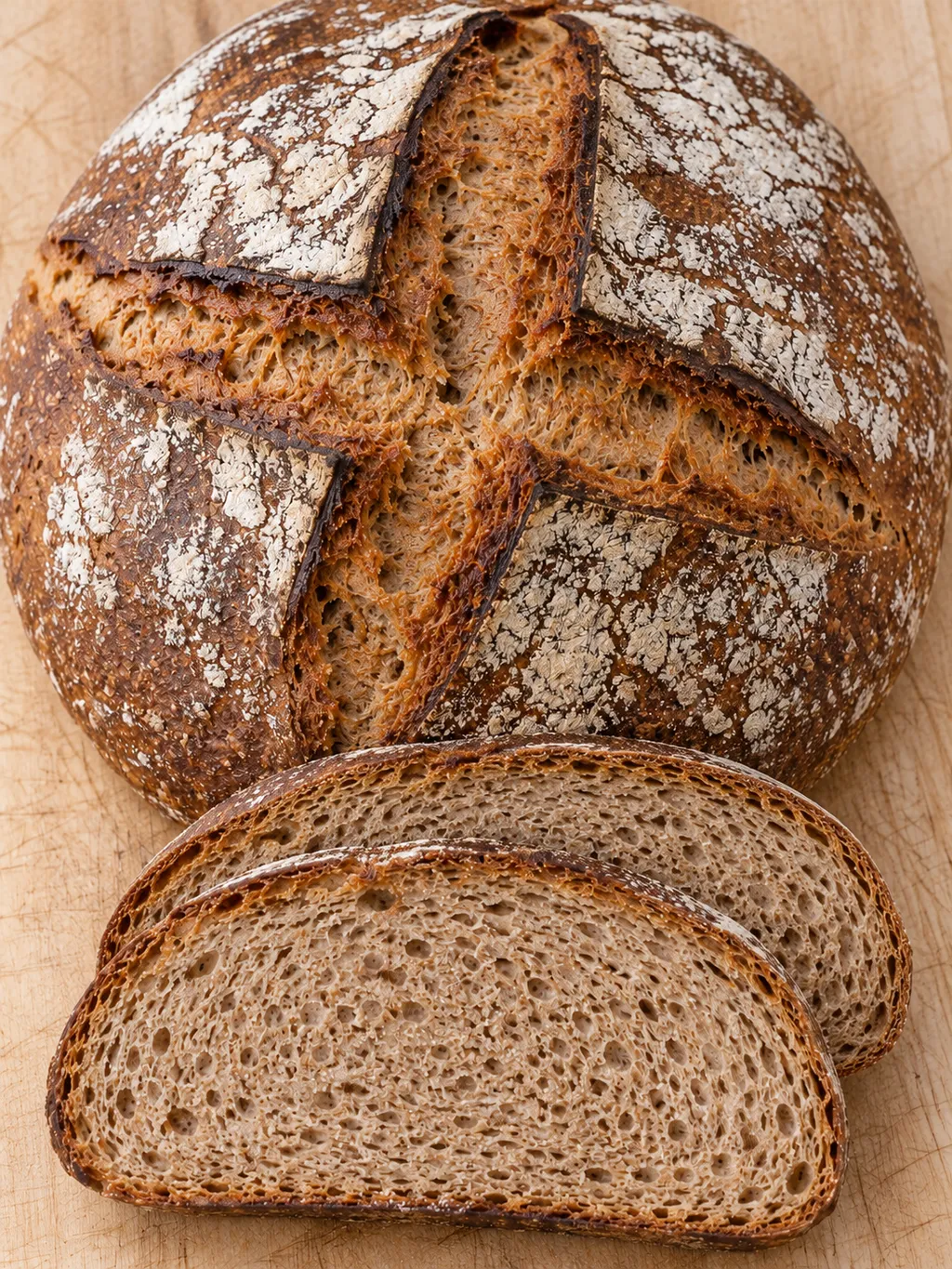 Rundes Bauernbrot mit kreuzförmiger Kruste und zwei aufgeschnittenen Scheiben