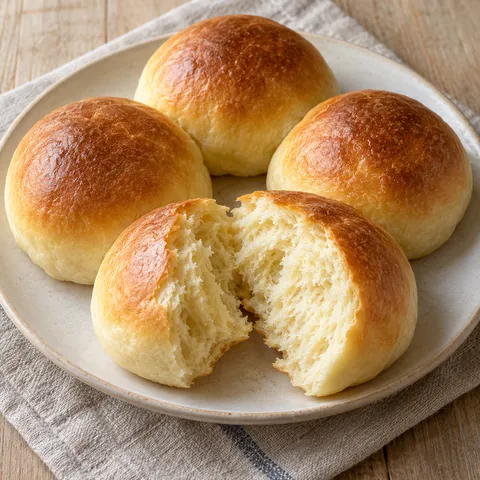 Goldbraune Milchbrötchen mit aufgebrochener, feinporiger Krume auf einem hellen Teller
